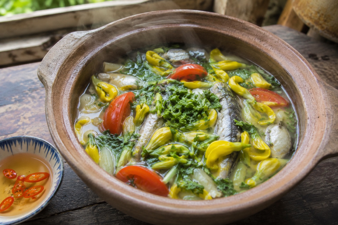 Nồi đất canh chua cá linh nấu bông điên điển còn bốc khói, bông vàng nổi kín mặt nước, bên cạnh chén nước mắm ớt