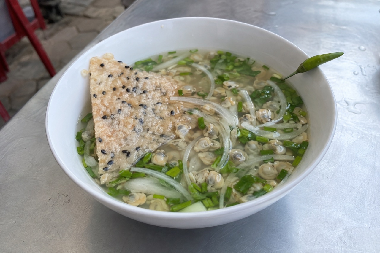 Chén don nước trong, thịt don nhỏ, hành lá và hành tây nổi bên trên, bánh tráng nướng bẻ vụn bỏ vô