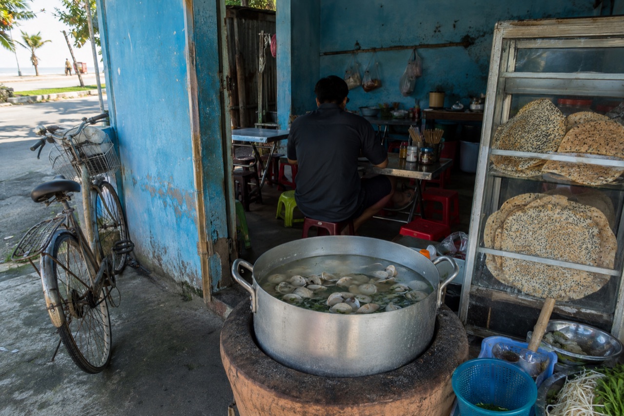 Quán don ven đường ở Quảng Ngãi, nồi nước luộc trên bếp, chồng bánh tráng trong tủ kiếng, ghế nhựa thấp