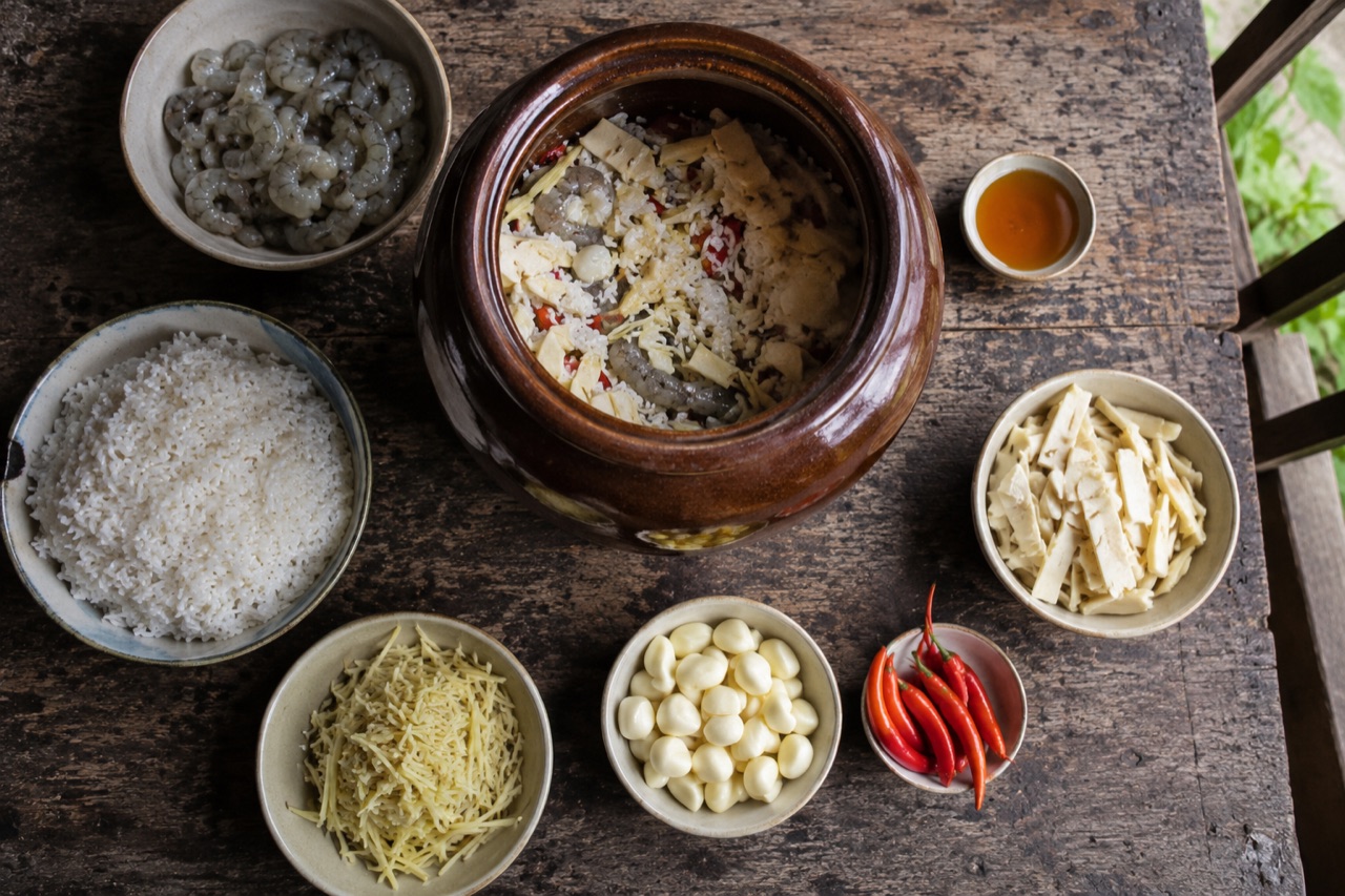 Bàn bếp xếp đồ vô hũ tôm chua: tôm sống đã lặt đầu, cơm nếp, riềng xắt sợi, tỏi lột, ớt, măng vòi và chén mật ong