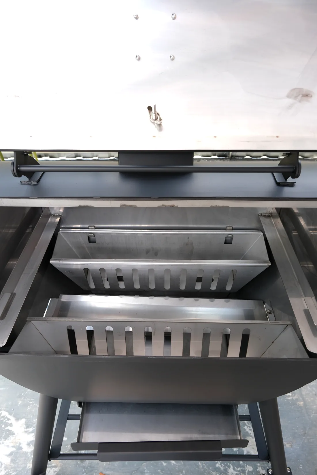 Nhìn từ trên xuống lòng cái lò nướng than tách khói 65L inox lúc mở nắp: hai hộc than dài bằng inox khoét khe nằm dọc mép trước và mép sau, giữa hai hộc là một khe dài còn để trống, cả hai hộc đều chưa nạp than.